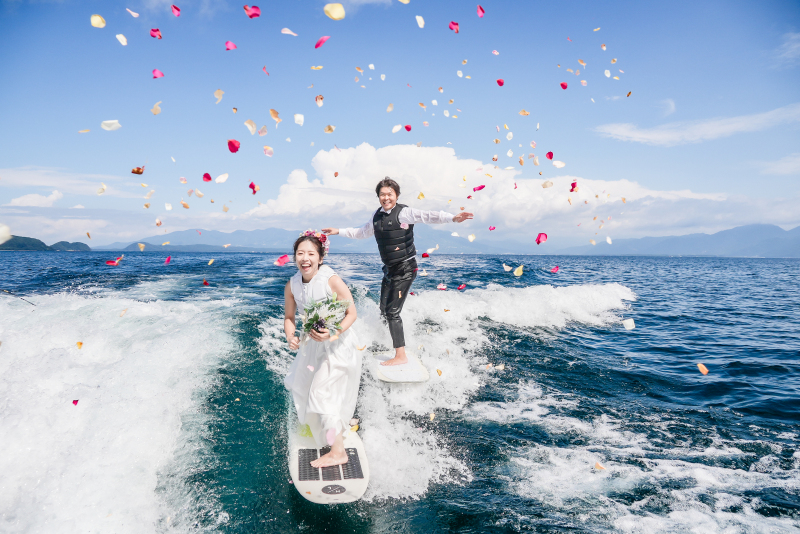 猪苗代湖にてモーターボートをチャーターしてお二人の趣味のウェイクサーフィンをしながらのフォトウェディング。ドレスはアクティブ用で安全面に配慮。フラワーシャワーは環境に配慮して生のお花を使いました。