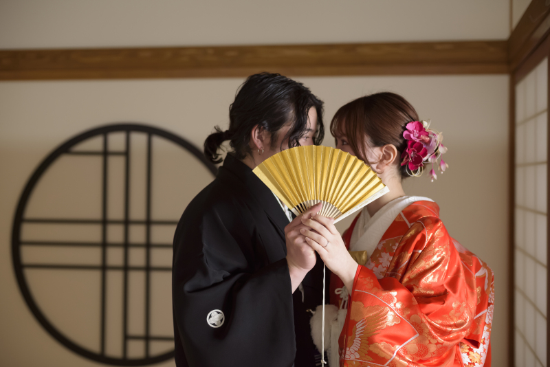 扇子越しに見つめ合う、華やかな和装フォト