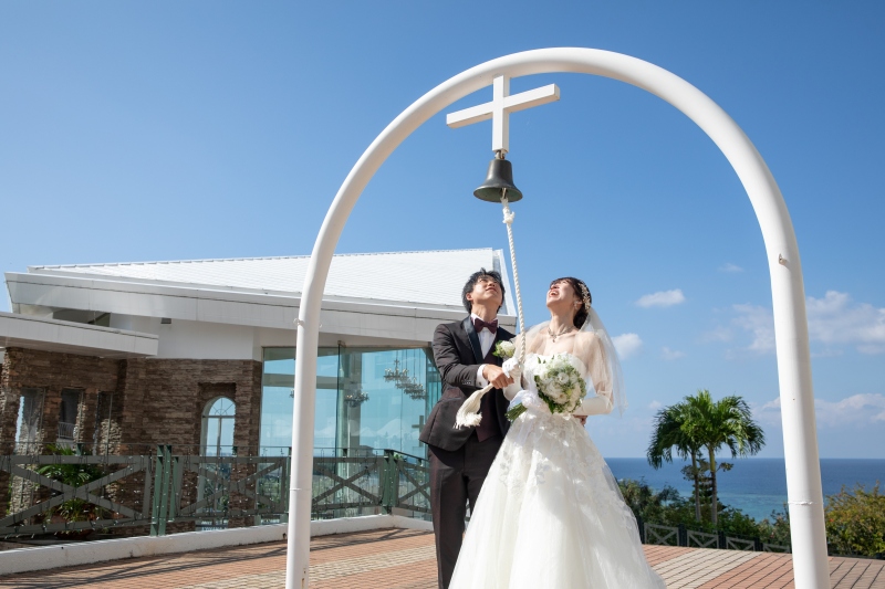 青空の下、チャペルをバックにベルを鳴らすふたり