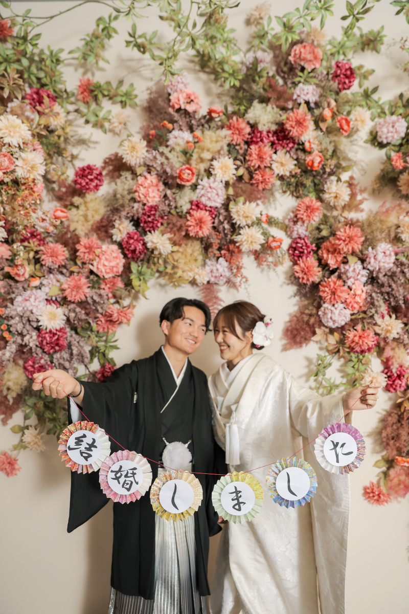 花咲く背景に掲げる「結婚しました」の記念フォト