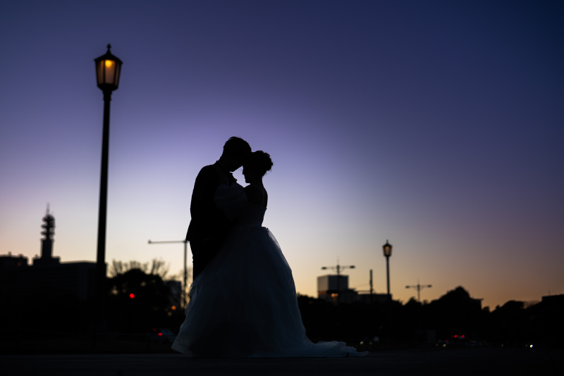 夕暮れの柔らかな光に照らされる街並みを背景にした、シルエット写真。ビルの輪郭や通りに差し込む光のグラデーションが、おふたりの姿をより美しく引き立てます。日常の景色も、夕日の魔法で特別な瞬間に。